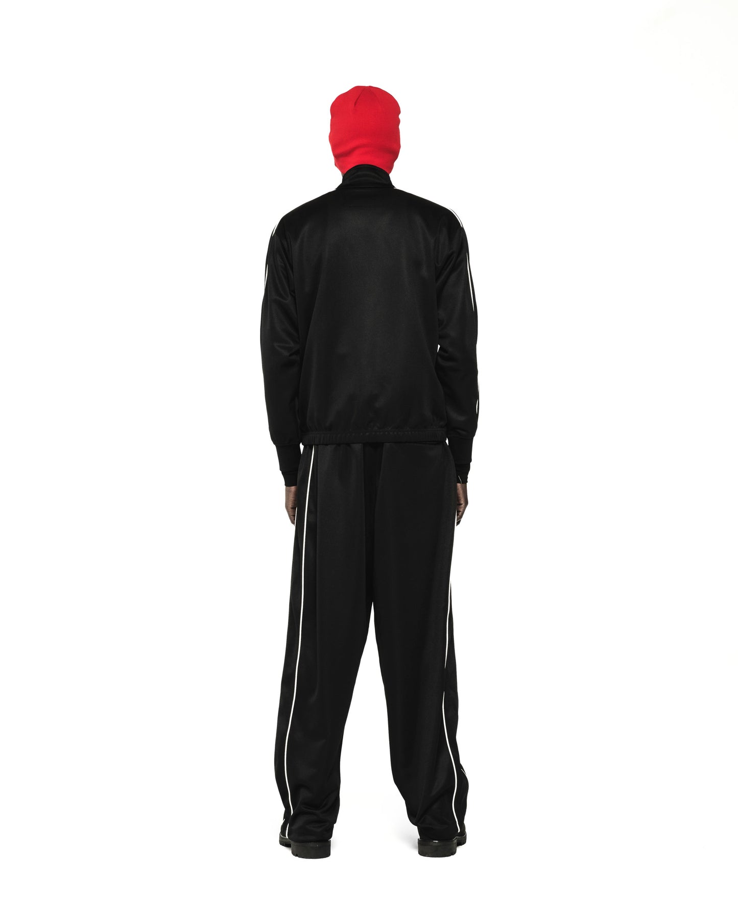 Black polyester track jacket and pants with white piping, worn by a figure in a red beanie.