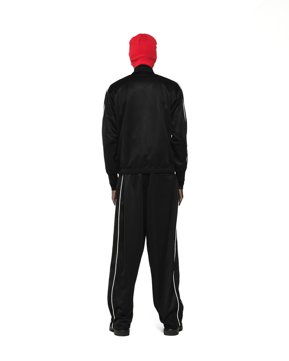 Black polyester track jacket and pants with white piping, worn by a figure in a red beanie.