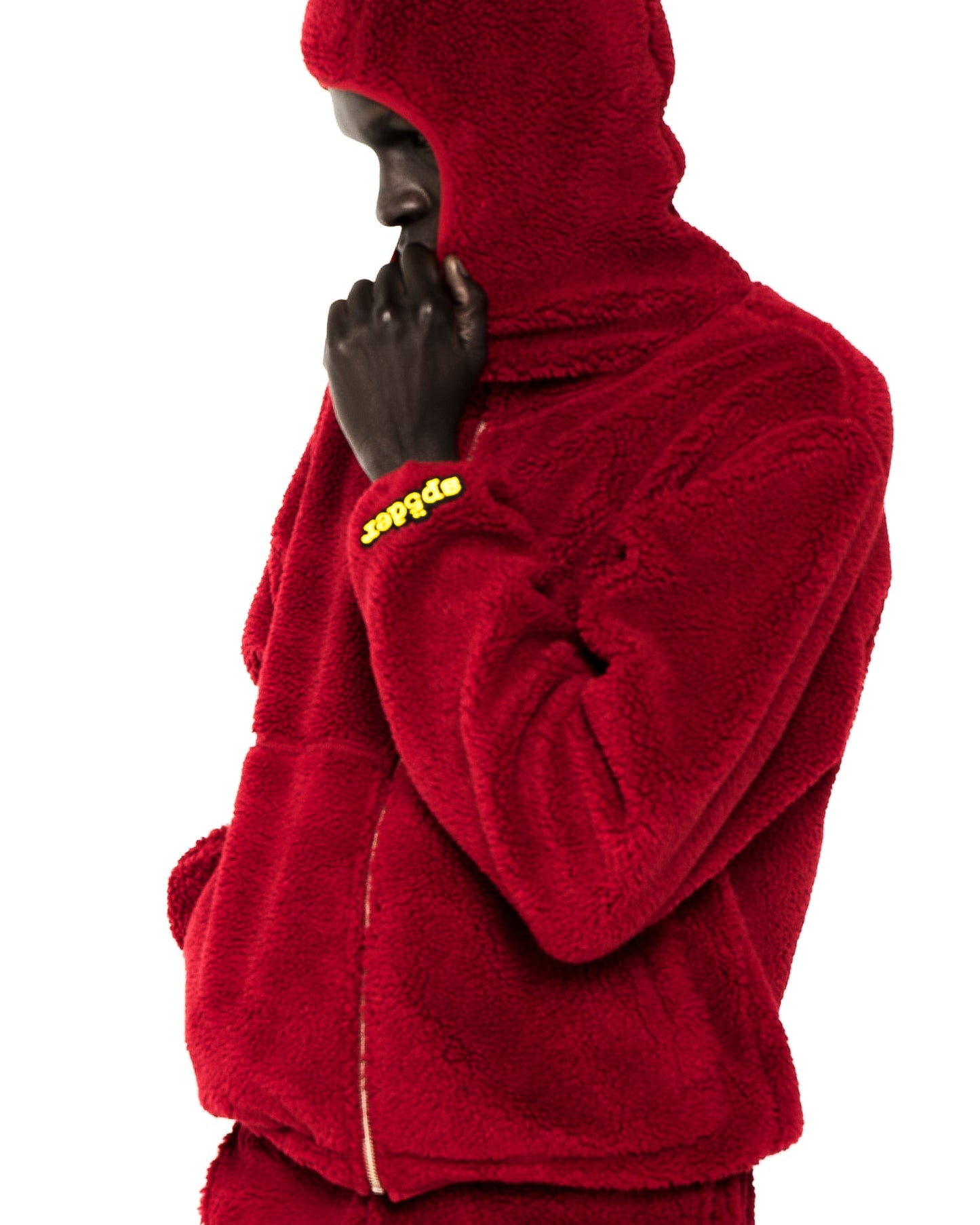 Red teddy fleece zip-up hooded jacket with a yellow rubberized logo patch on the wrist.