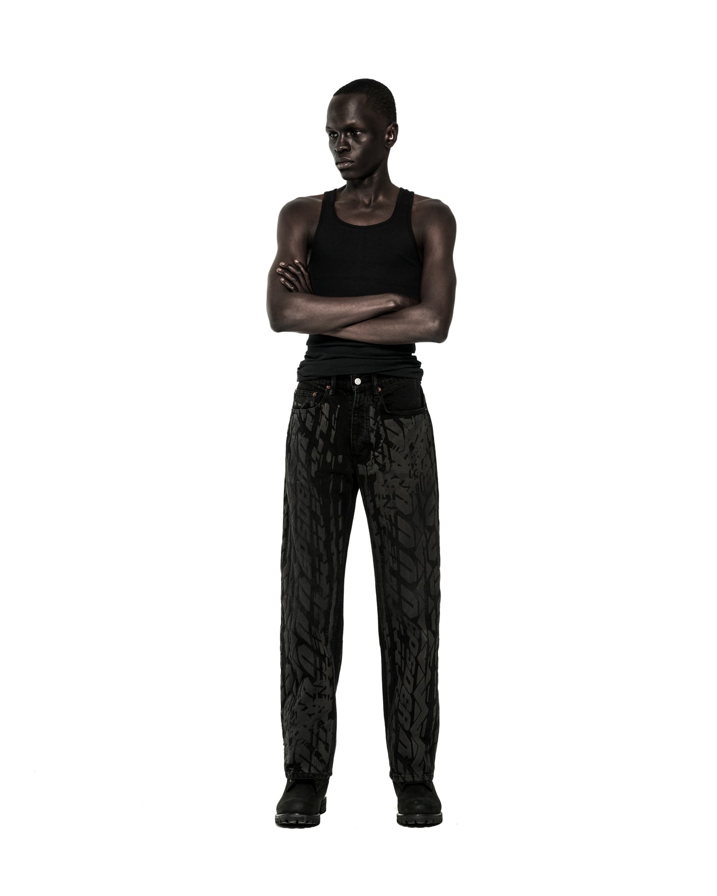 Dark-skinned model in black tank top and black Burnout Denim pants with all-over tire track design.