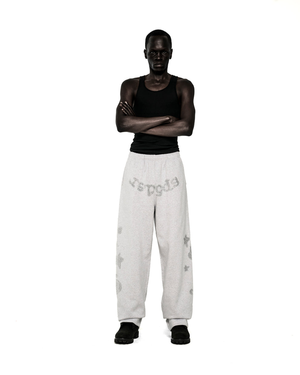 Model wearing light grey rhinestone-embellished wide-leg sweatpants with "SP5DER" text, "5", and star designs.