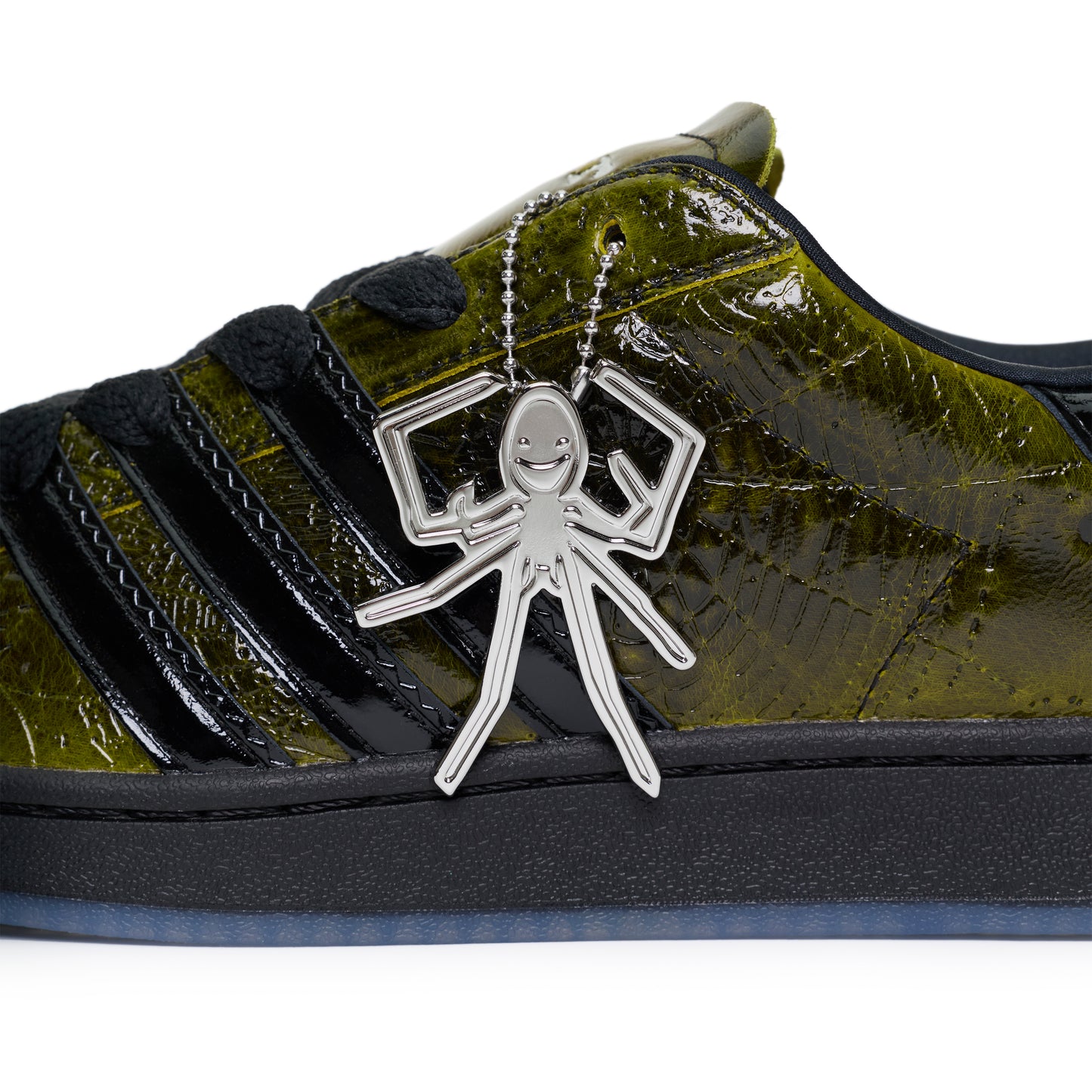 SP5DER x ADIDAS SUPERSTAR with glossy cracked olive patent leather upper, black stripes, and a silver spider charm.