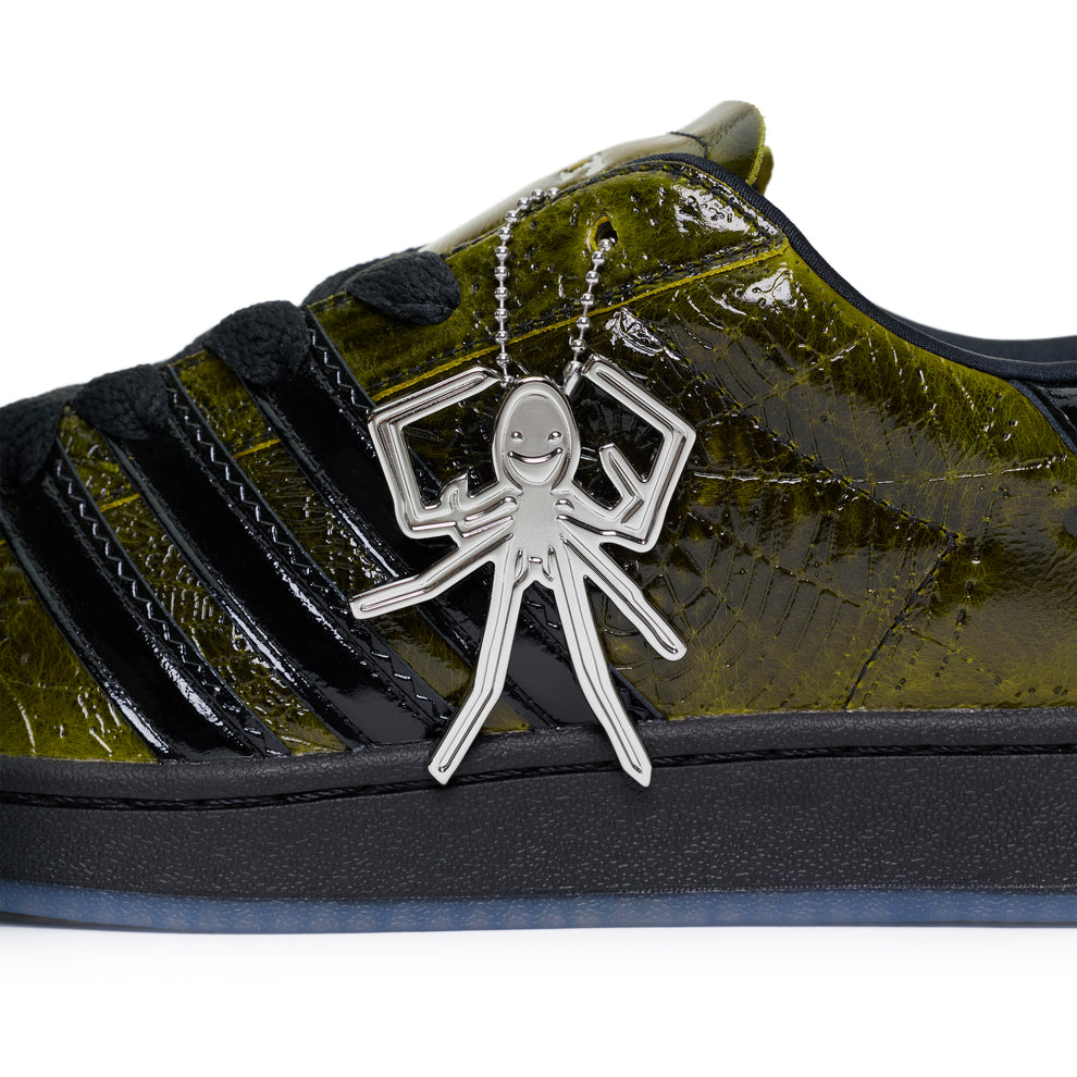 SP5DER x ADIDAS SUPERSTAR with glossy cracked olive patent leather upper, black stripes, and a silver spider charm.
