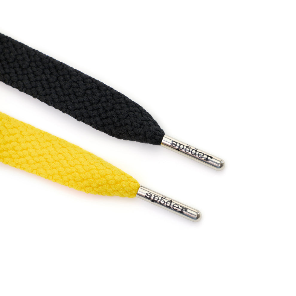 Close-up of black and yellow flat woven shoelaces with silver aglets embossed with "sp5der".