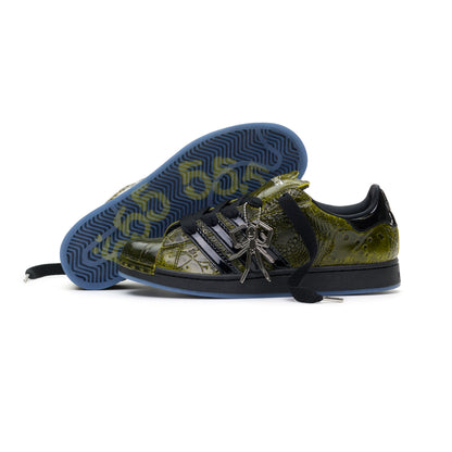 SP5DER x ADIDAS SUPERSTAR in glossy cracked olive patent leather with black stripes, spider charm, and blue translucent sole.