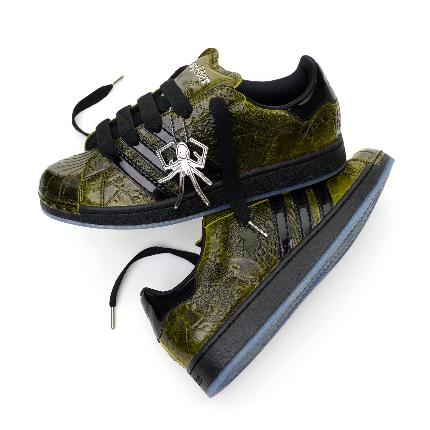 SP5DER x ADIDAS SUPERSTAR sneakers: glossy cracked olive patent leather, black stripes, spider charm, and translucent outsole.