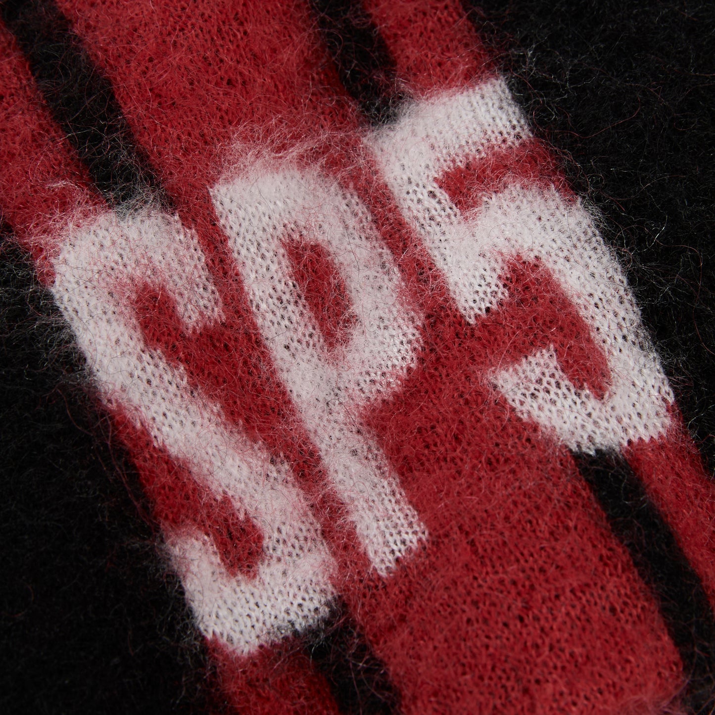 RALLY BEANIE: Close-up of black and red mohair knit with white "SP5" logo and vertical stripes.