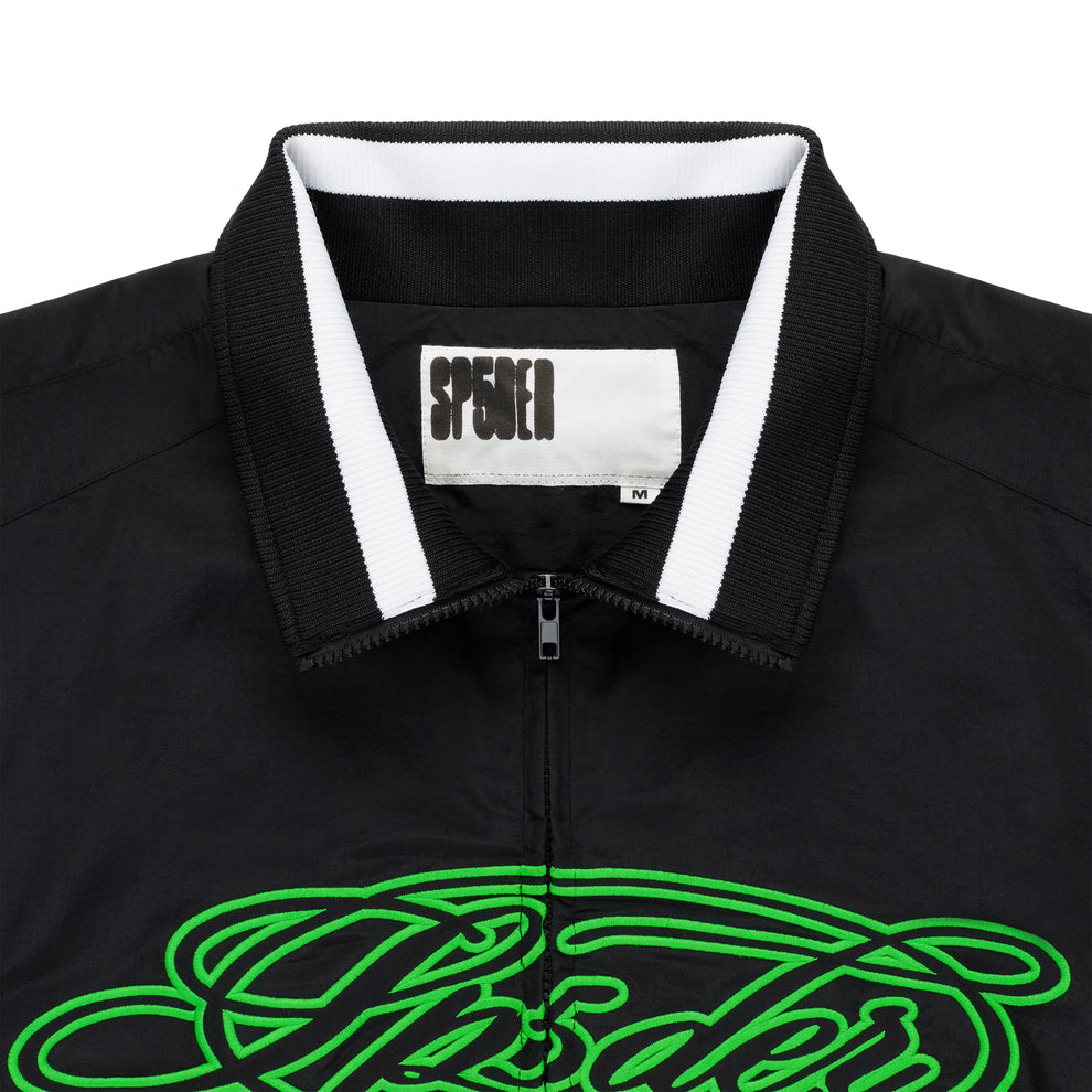 Black nylon track jacket with full zip, stand collar, white stripe detail, and green embroidered script logo.