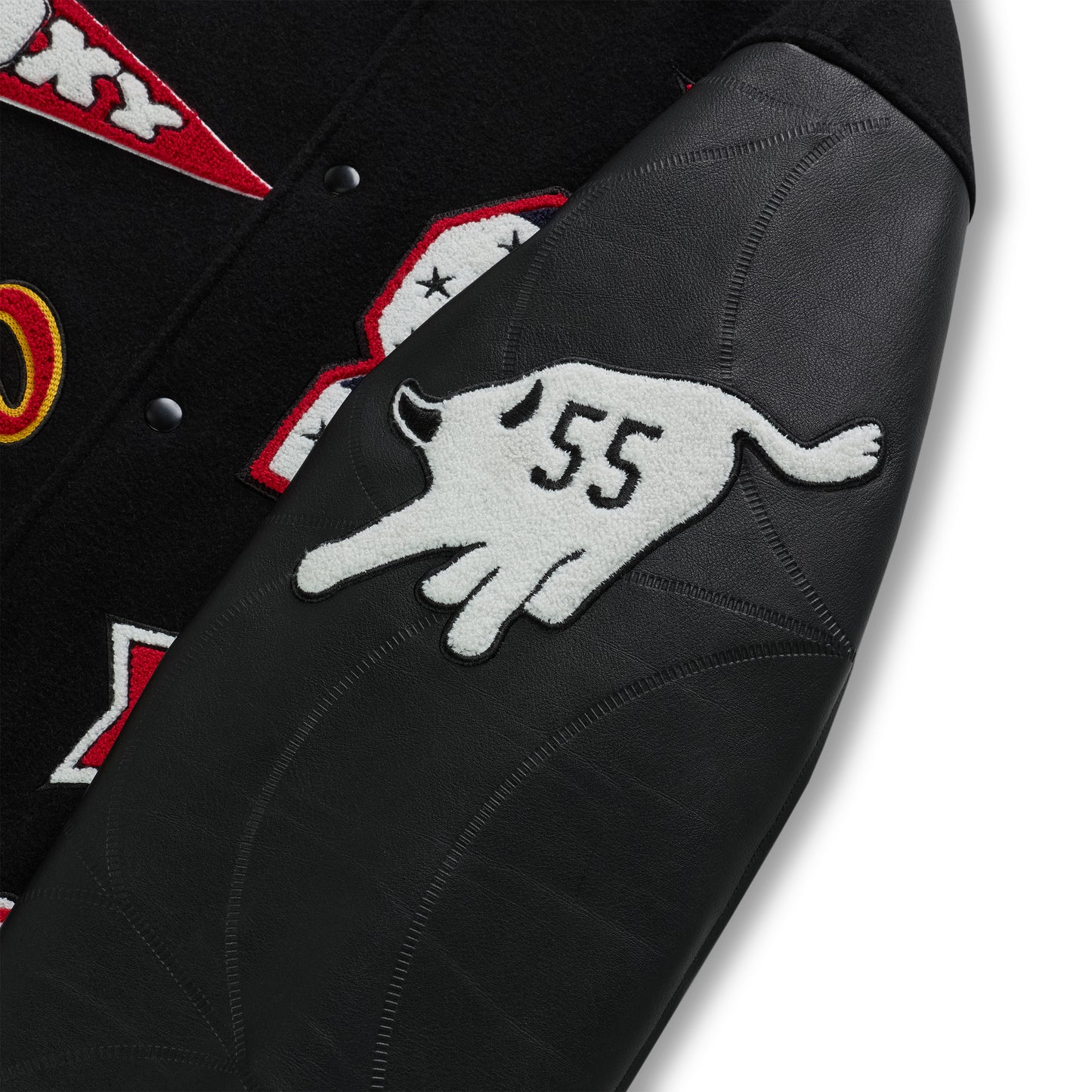 Black wool varsity jacket with contrasting debossed leather sleeves, embroidered patches, and striped ribbed trim.