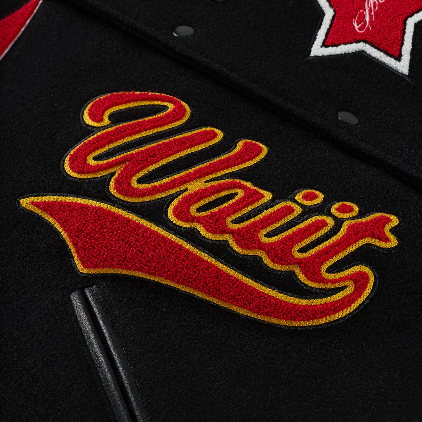 Black wool varsity jacket with red and yellow embroidered "Waiir" patch and leather sleeve detail.