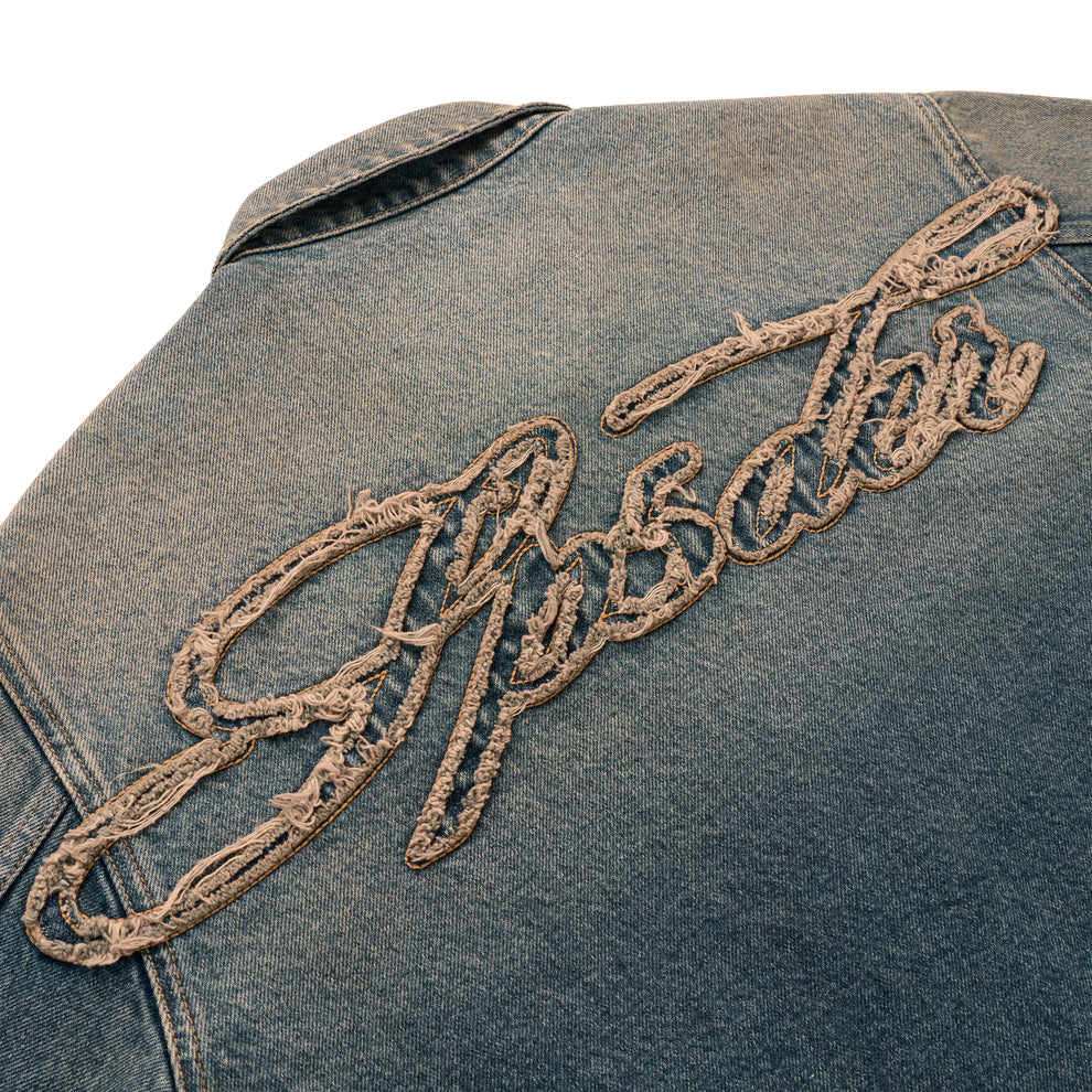Blue denim work jacket with "Script" embroidered in distressed beige thread on the back.