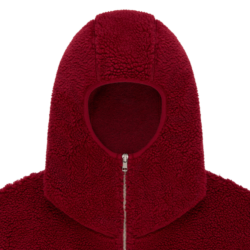 Close-up of a red sherpa fleece hooded jacket with a narrow front opening and silver zip closure.