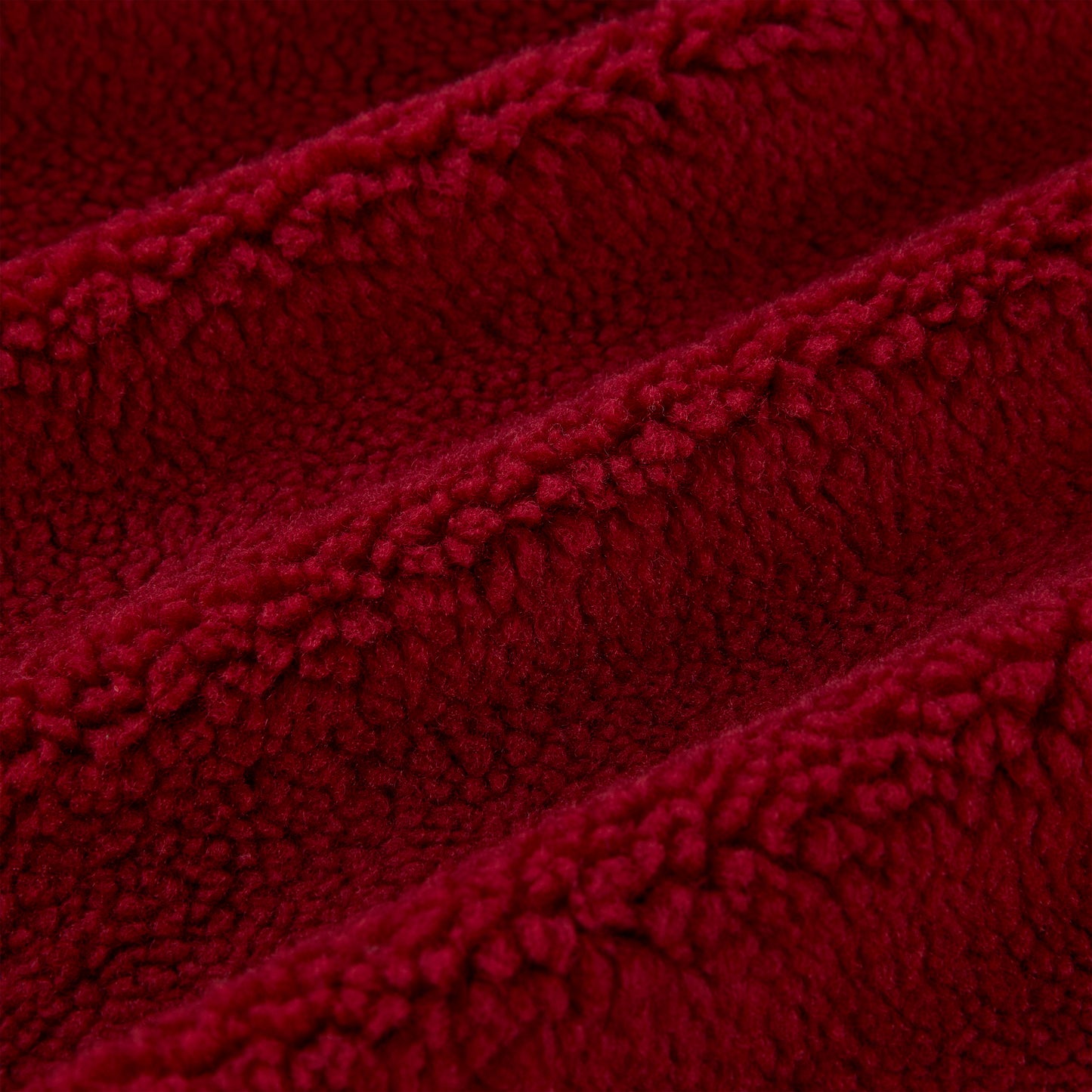 Close-up of plush red teddy sherpa fleece fabric with soft, textured loops and gentle folds.