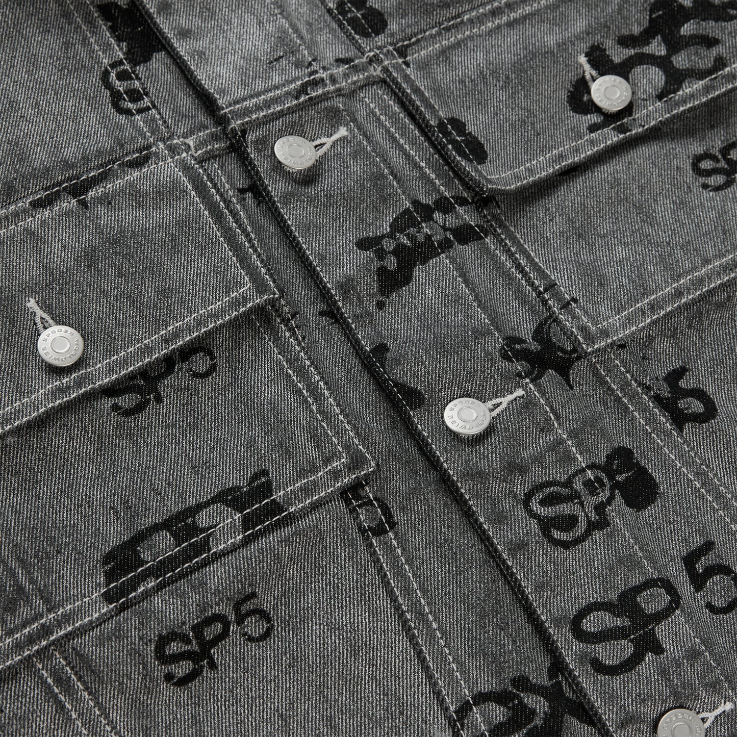 Gray denim trucker jacket with all-over black foil print, silver buttons, and red contrast stitching.