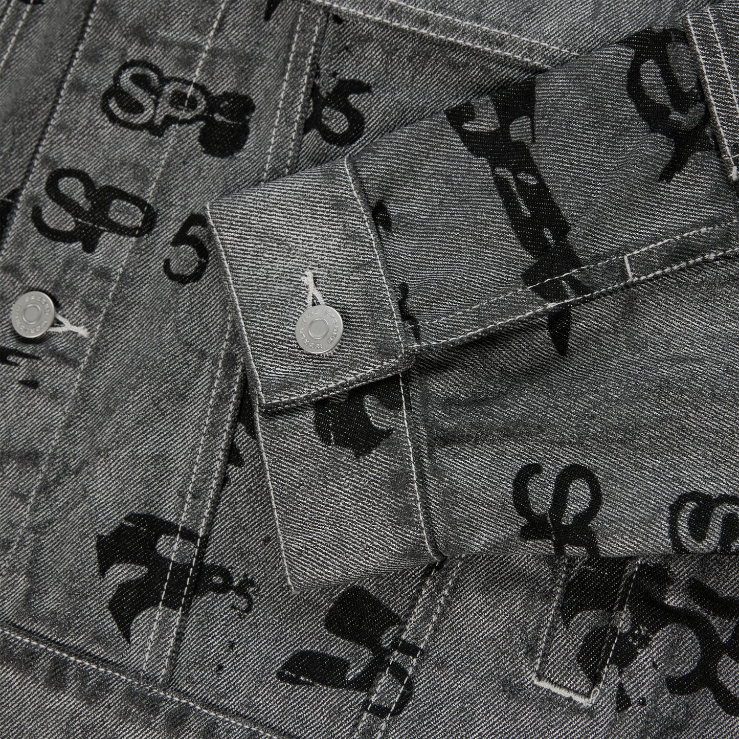 Gray denim trucker jacket with black all-over print, silver buttons, and red contrast stitching.