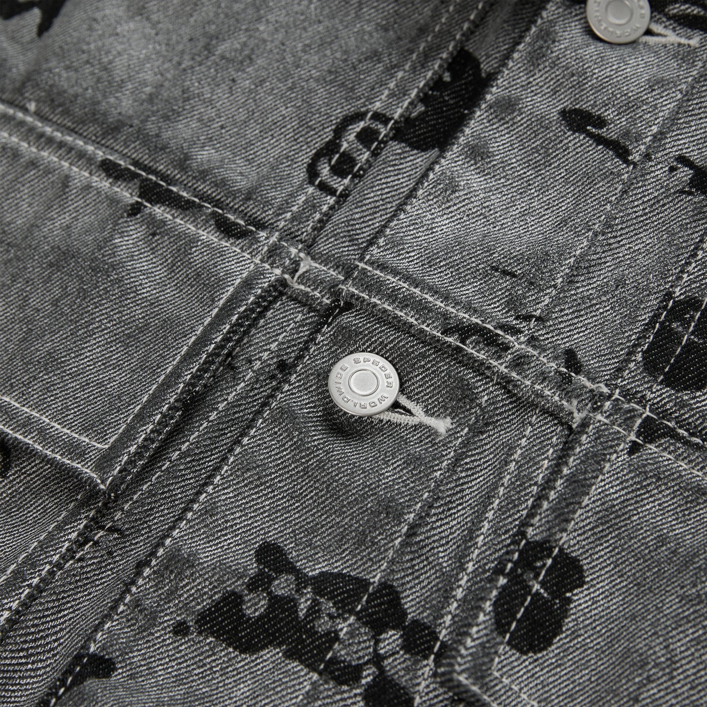 Close-up of a black denim trucker jacket with an all-over print, silver buttons, and red contrast stitching.