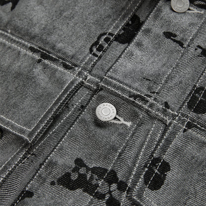 Close-up of a black denim trucker jacket with an all-over print, silver buttons, and red contrast stitching.
