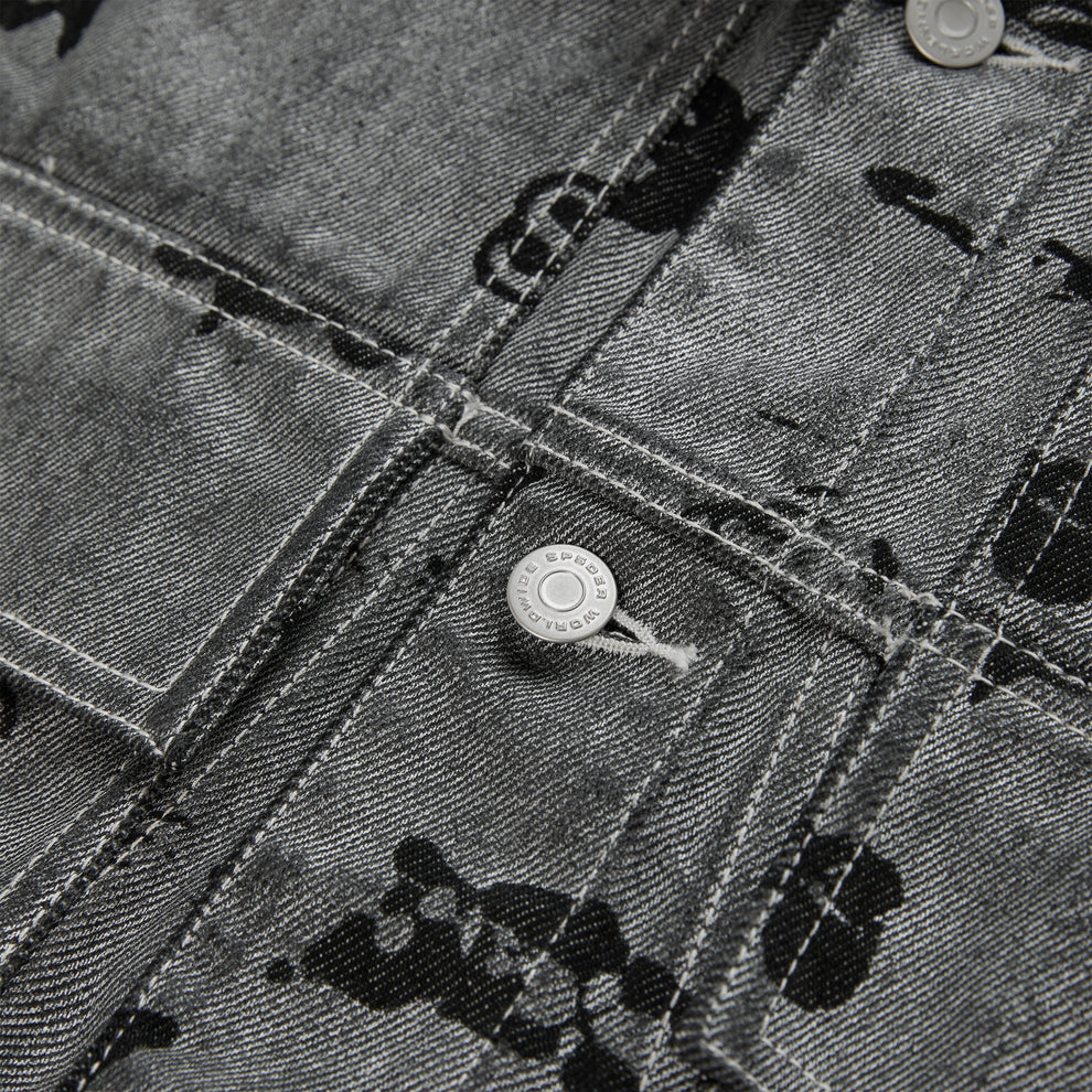 Close-up of a black denim trucker jacket with an all-over print, silver buttons, and red contrast stitching.