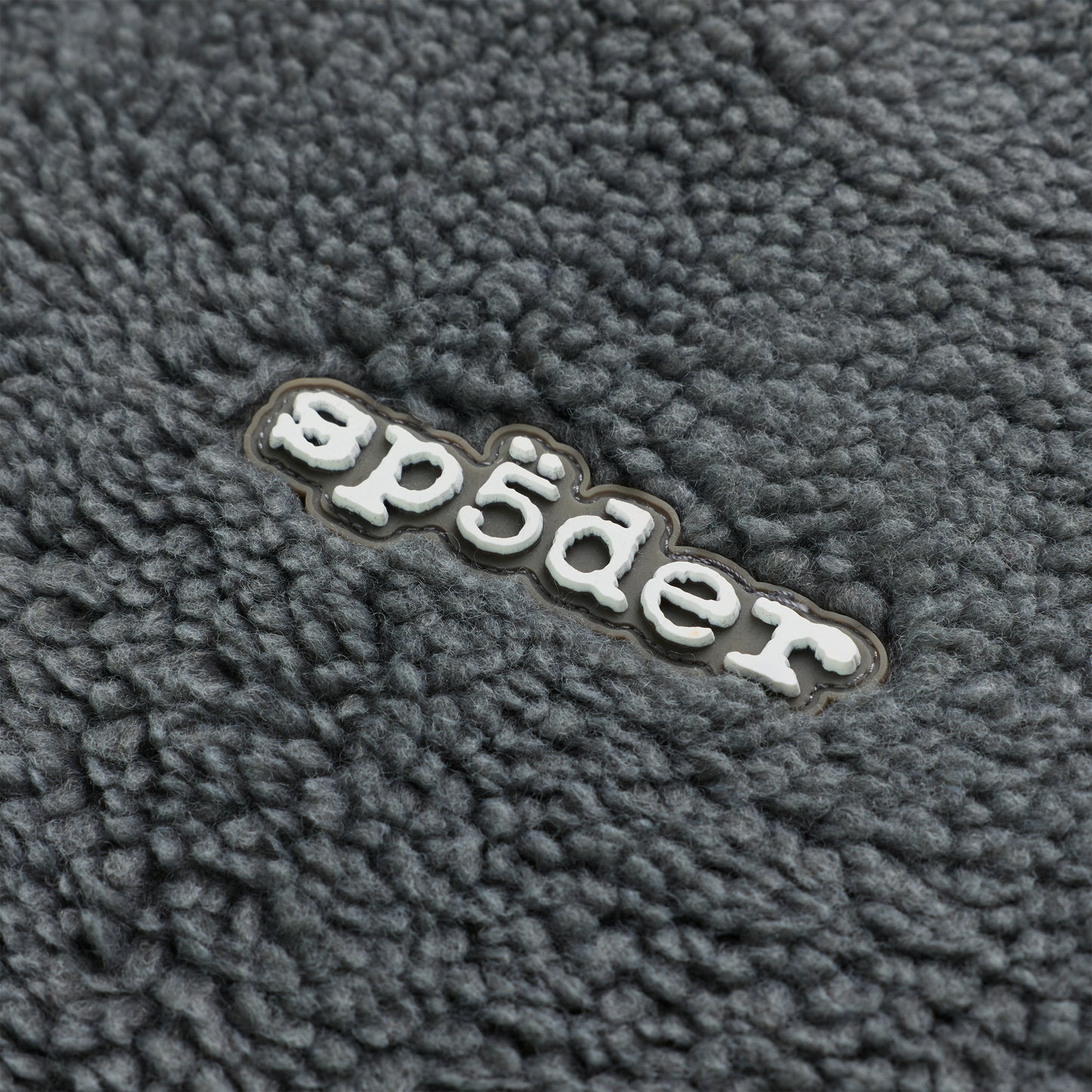 Close-up of gray sherpa fleece with a white rubberized "sp5der" logo patch.