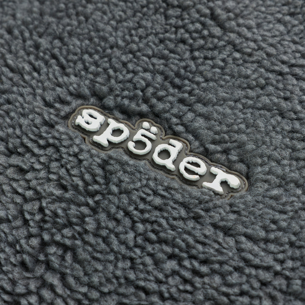 Close-up of gray sherpa fleece with a white rubberized "sp5der" logo patch.