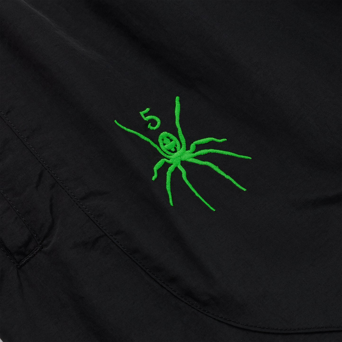 Black nylon track pant with a vibrant green embroidered spider and "5" graphic.