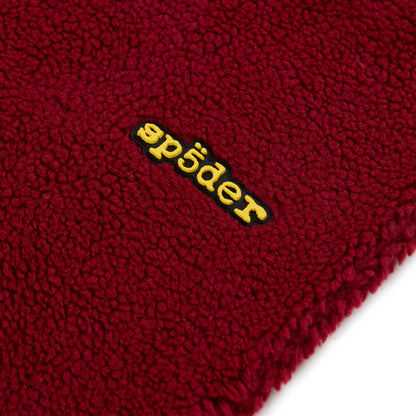 Close-up of a red teddy fleece pant with a yellow rubberized "sp5der" logo patch.