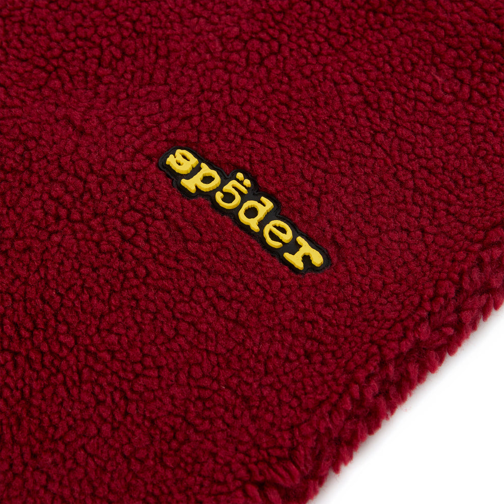Close-up of a red teddy fleece pant with a yellow rubberized "sp5der" logo patch.