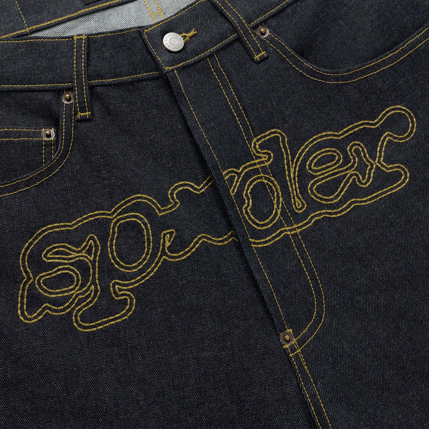 Dark wash denim jeans with yellow embroidered "SP5DER" logo across the crotch.