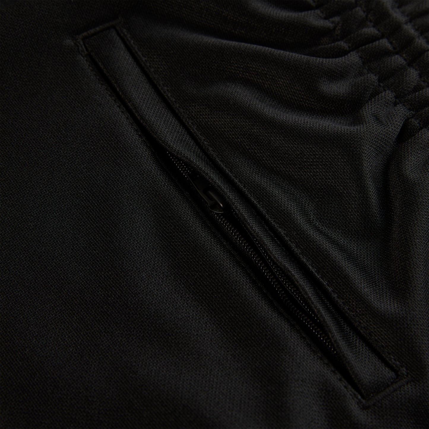 Close-up of black ATLANTA TRACK PANT, showing zippered pocket and elastic waistband.