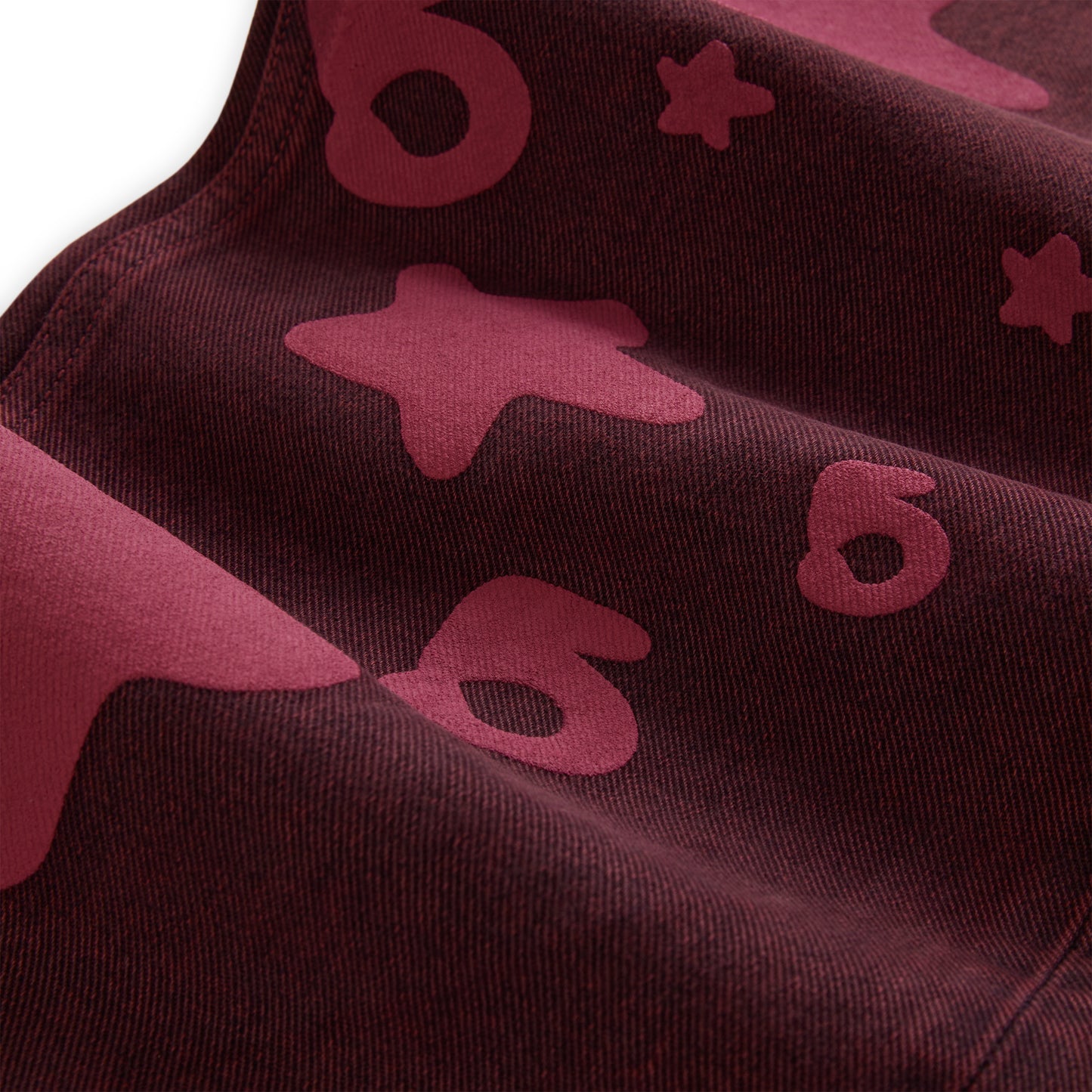 Close-up of BELUGA DENIM in faded wash, featuring dark red fabric with lighter red Beluga print stars and shapes.