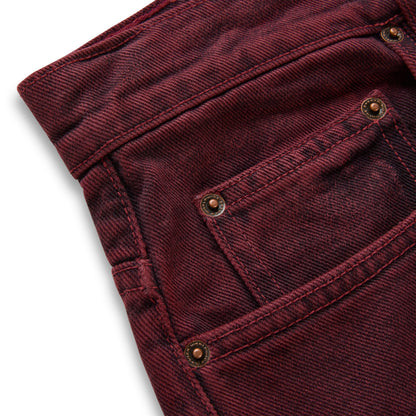 Faded wash burgundy denim pants with custom branded hardware and five-pocket styling.