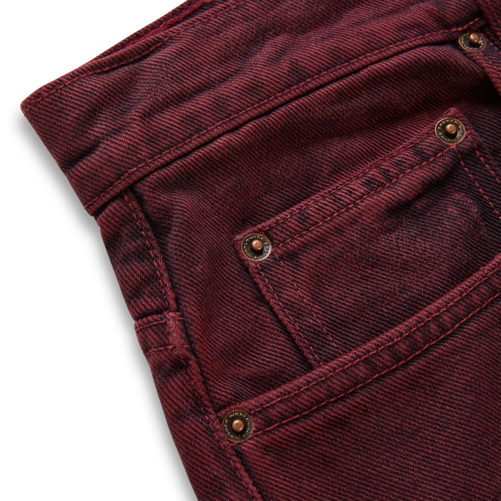 Faded wash burgundy denim pants with custom branded hardware and five-pocket styling.