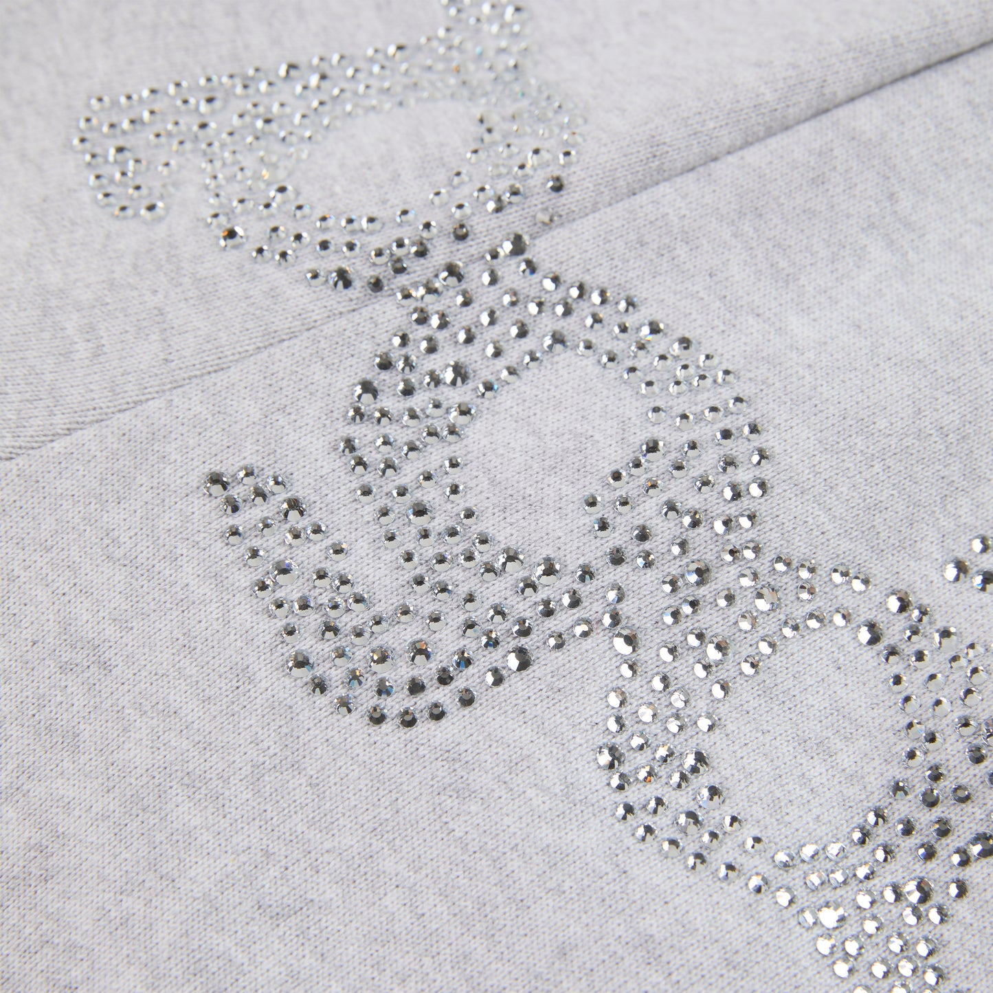 Close-up of gray cotton fleece sweatpants with "SP5DER" text and "5" star design in rhinestones.