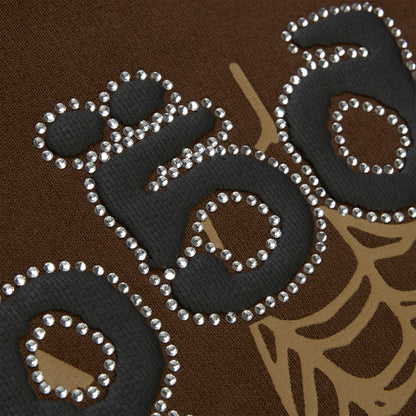 Close-up of brown cotton fleece hoodie with black puff print, rhinestone web, and text detail.