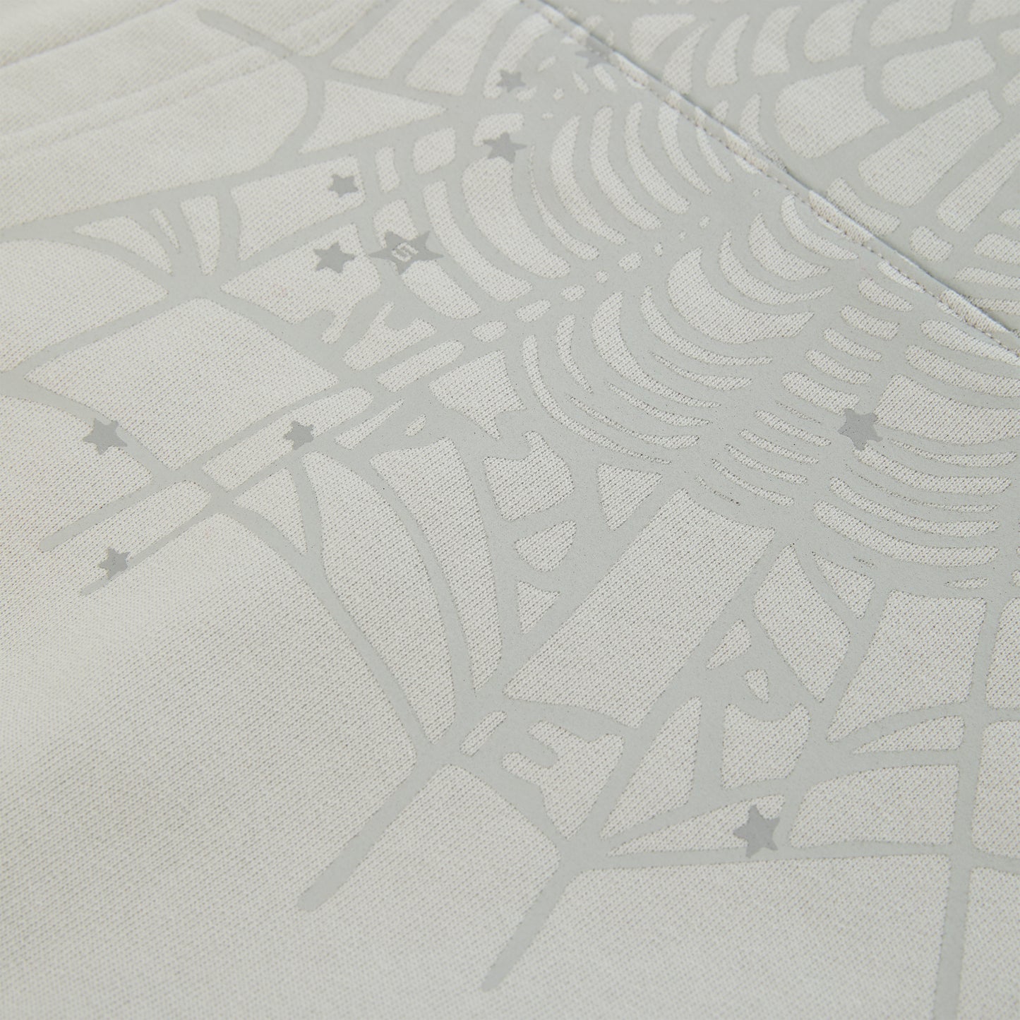 Close-up of a light gray cotton fleece hoodie with a subtle spiderweb and scattered star print.