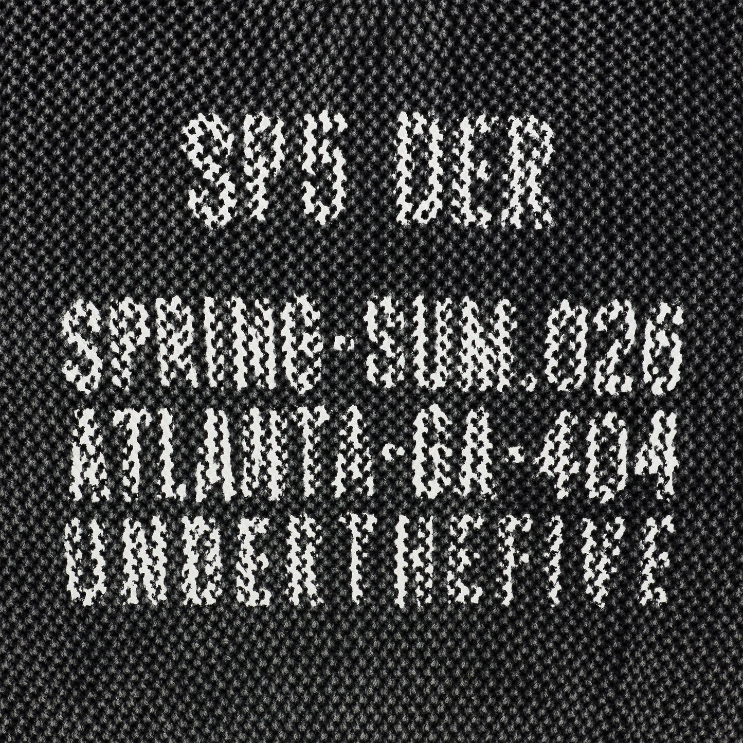 Black knit cotton sweater with white "UNDERTHEFIVE" text print and other details at chest.