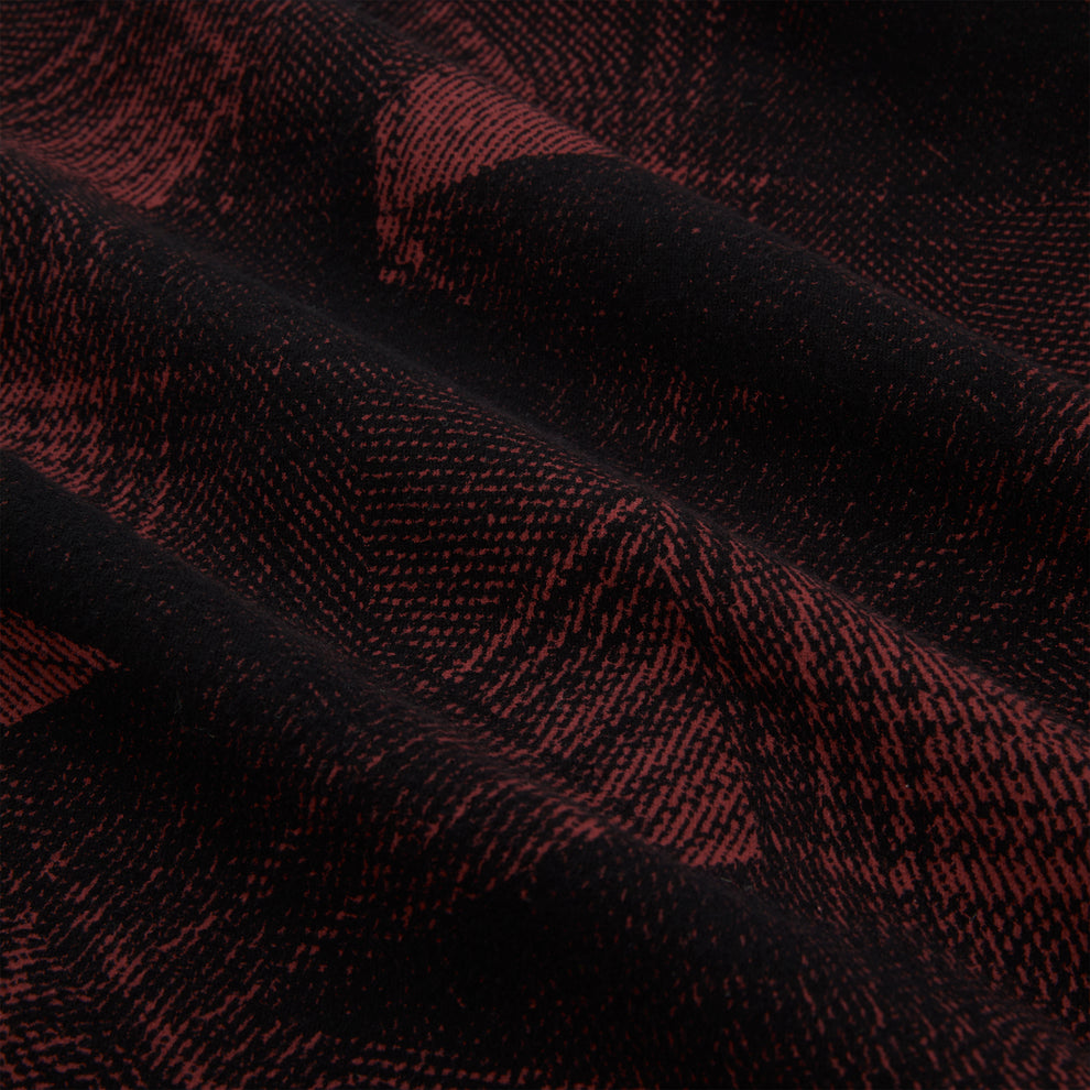 Close-up of black and red plaid cotton flannel fabric with SP5 graphic, showing soft texture and folds.