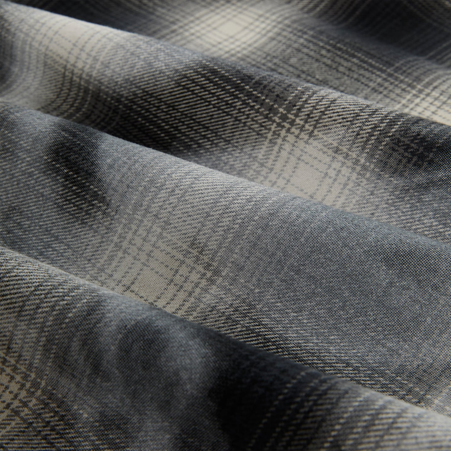 Close-up of a gray and cream cotton flannel shirt with a faded plaid graphic print.