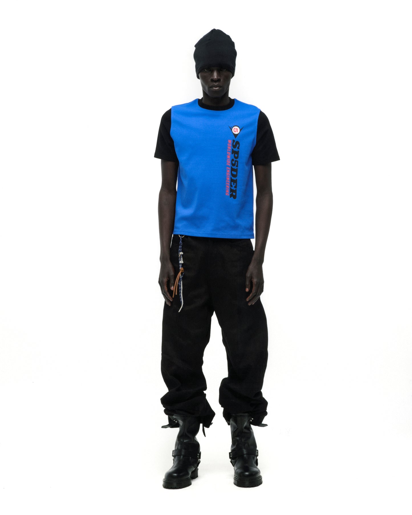Black model wearing a blue and black ENGINEER TEE with graphic print, black pants, and boots.