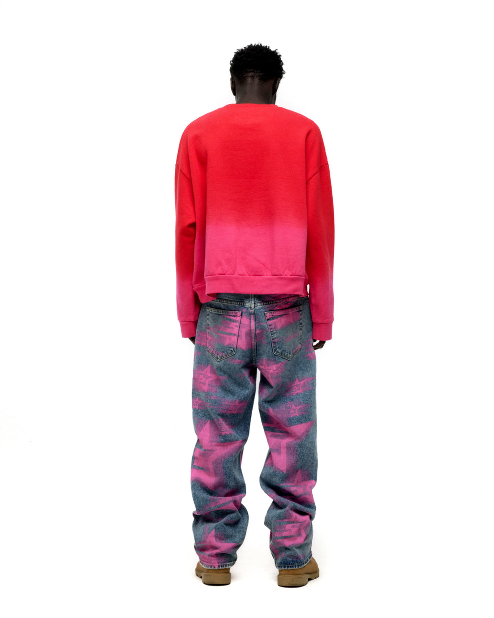 Man from behind wearing a red to pink gradient crewneck and blue jeans with pink star patterns.