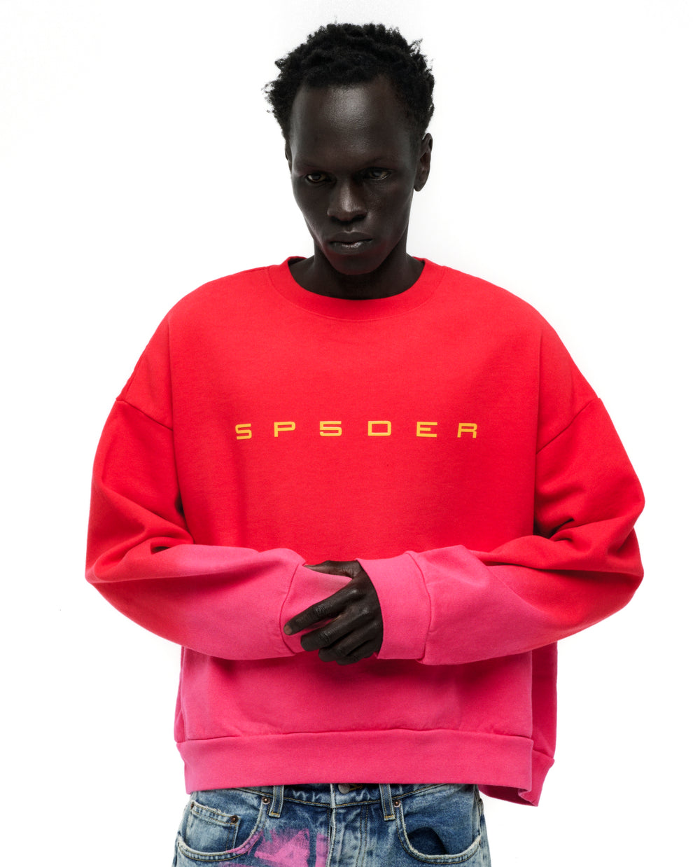 Red and pink gradient crewneck with yellow "SP5DER" text on chest, worn by a model.