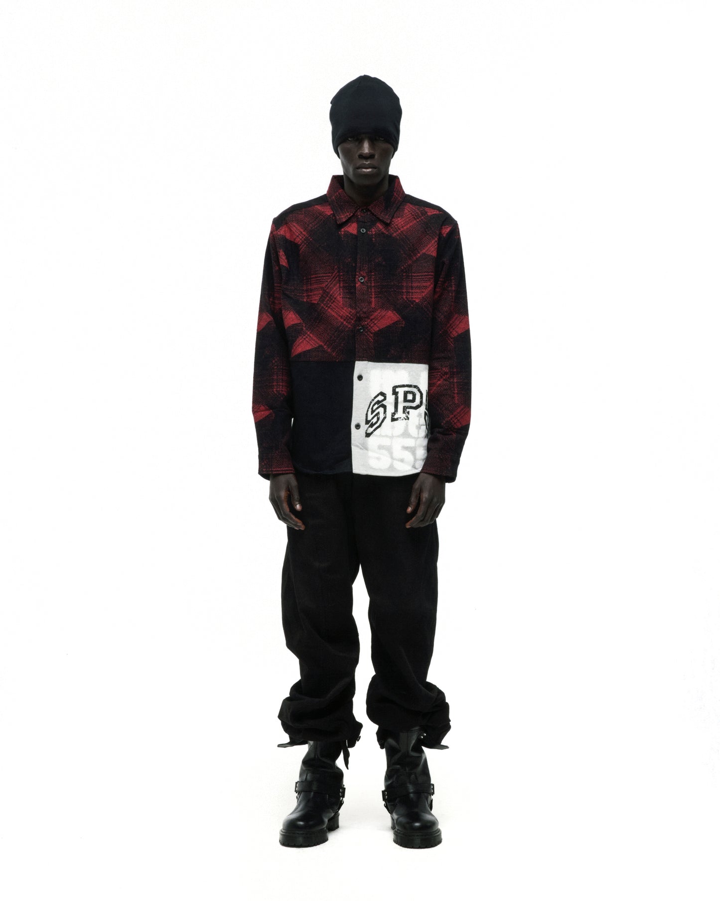 Black beanie, red and black plaid flannel shirt with SP5 graphic, black pants, and black boots.