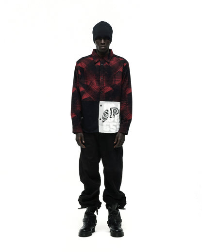 Black beanie, red and black plaid flannel shirt with SP5 graphic, black pants, and black boots.