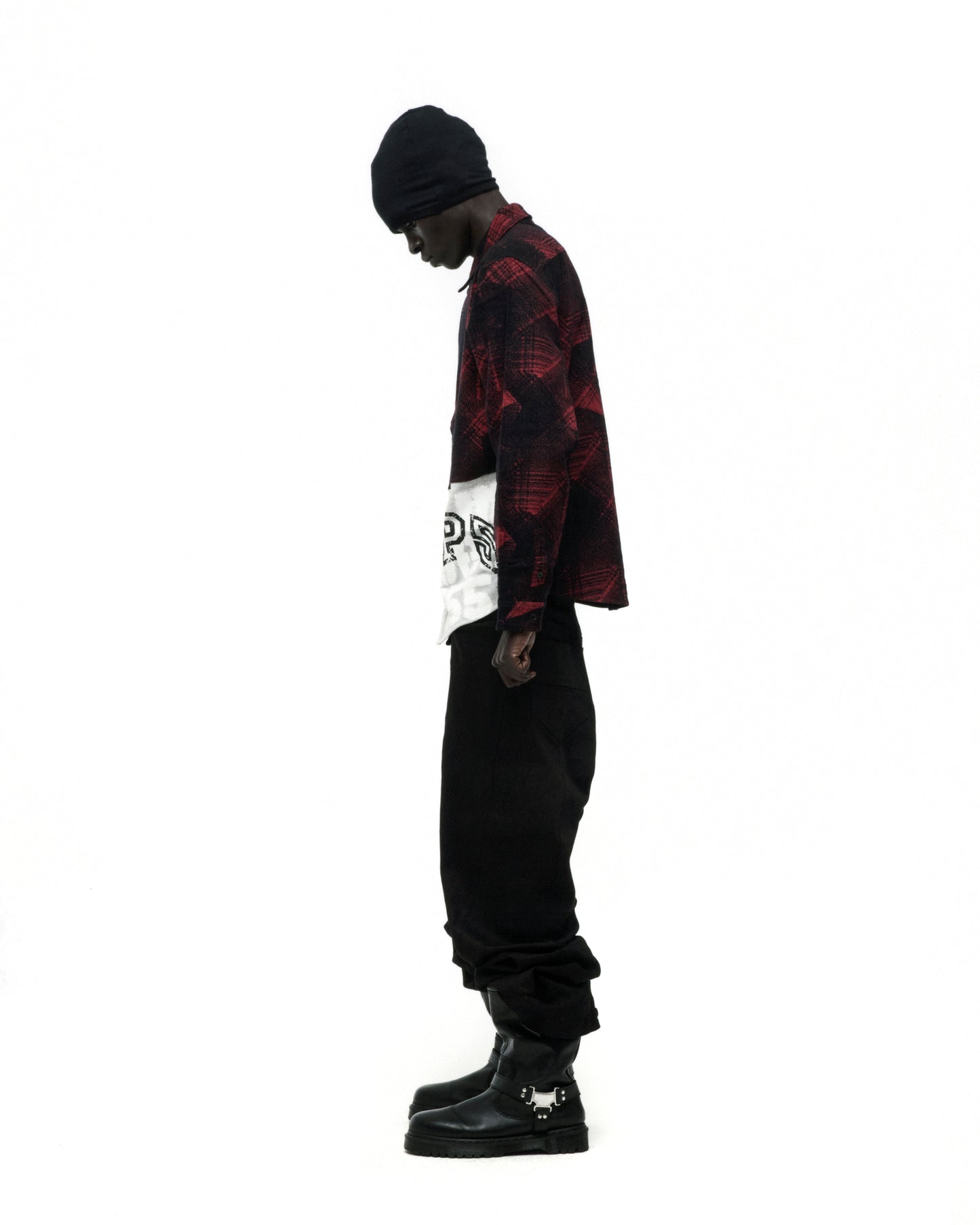 Man in red plaid cotton flannel shirt with SP5 graphic, black pants, beanie, and buckled boots.