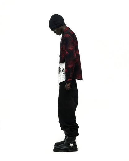 Man in red plaid cotton flannel shirt with SP5 graphic, black pants, beanie, and buckled boots.