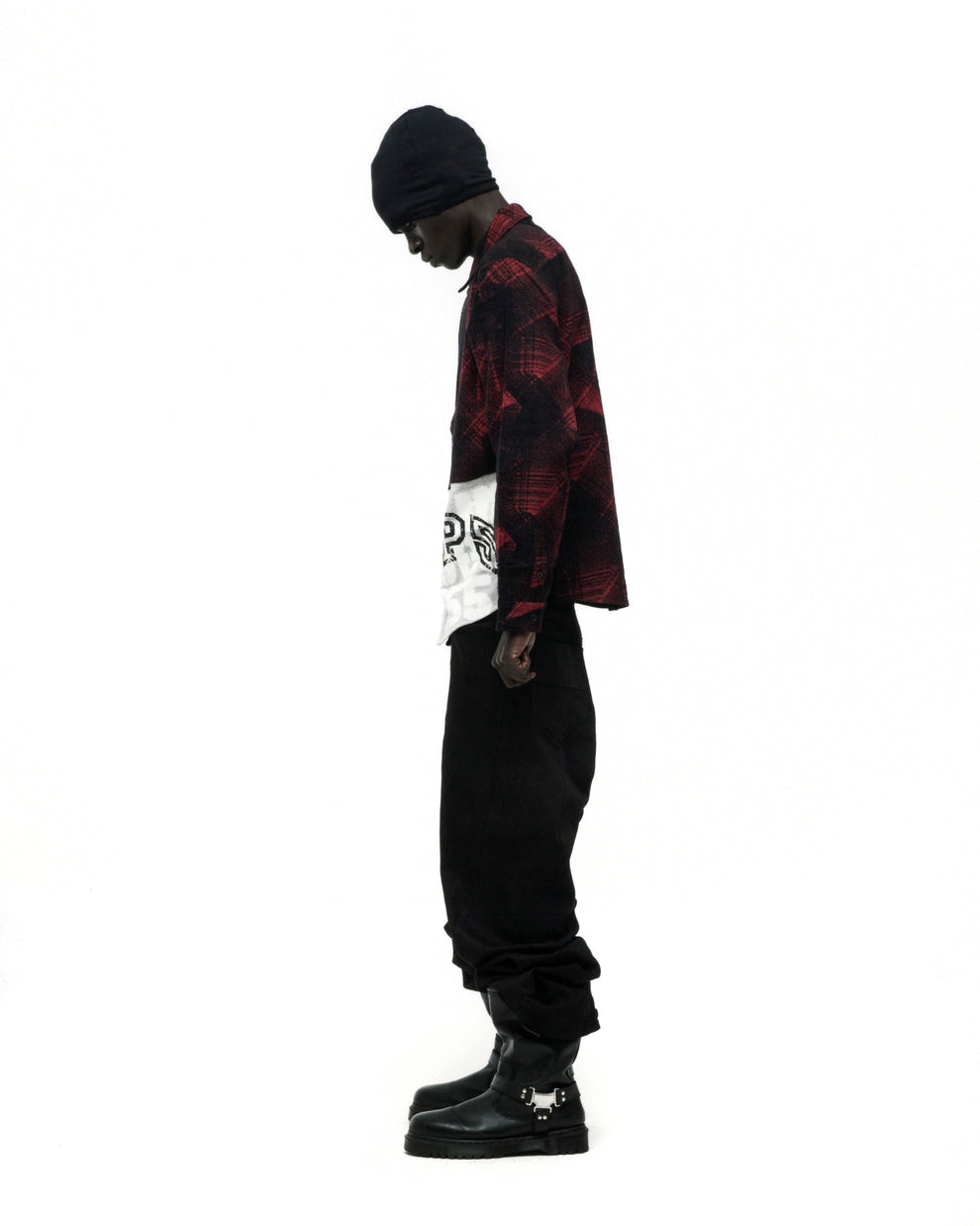 Man in red plaid cotton flannel shirt with SP5 graphic, black pants, beanie, and buckled boots.