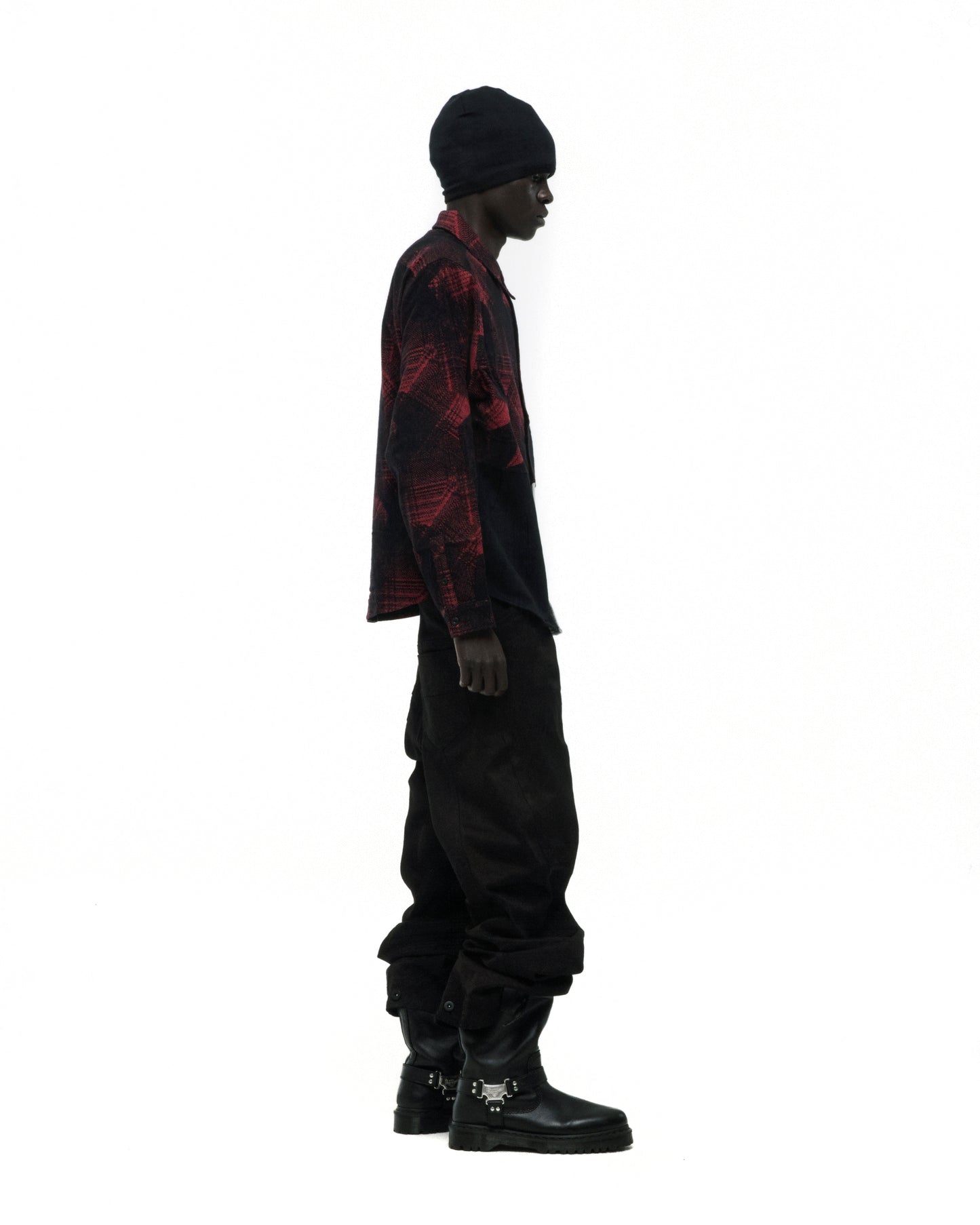 Model in red and black plaid cotton flannel shirt with SP5 graphic, black pants, beanie, and buckle boots.