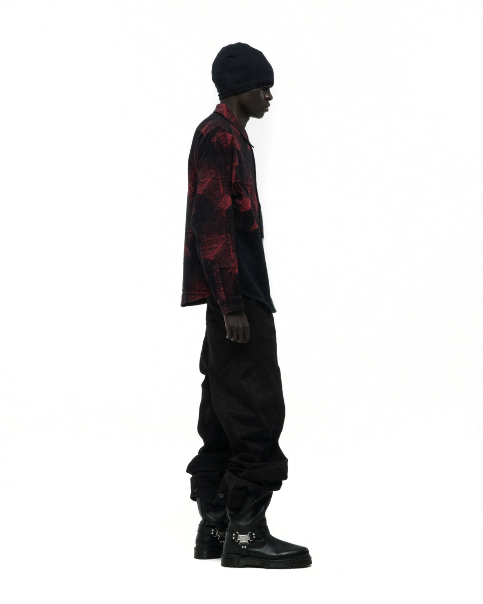 Model in red and black plaid cotton flannel shirt with SP5 graphic, black pants, beanie, and buckle boots.