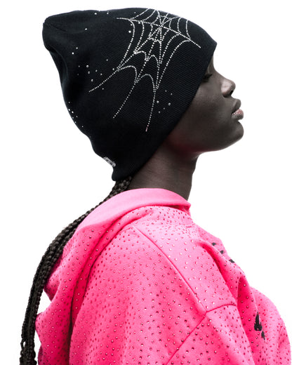 Black acrylic beanie with rhinestone spiderweb and skull designs, worn by a model.