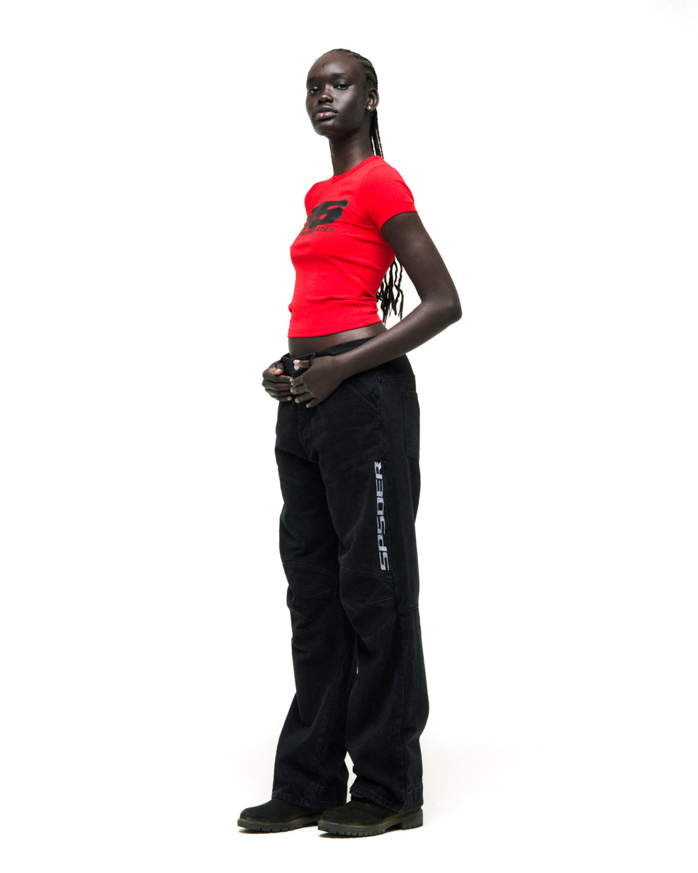 Model in red MOTO 5 BABY TEE with black graphic, paired with black SP5DER cargo pants.